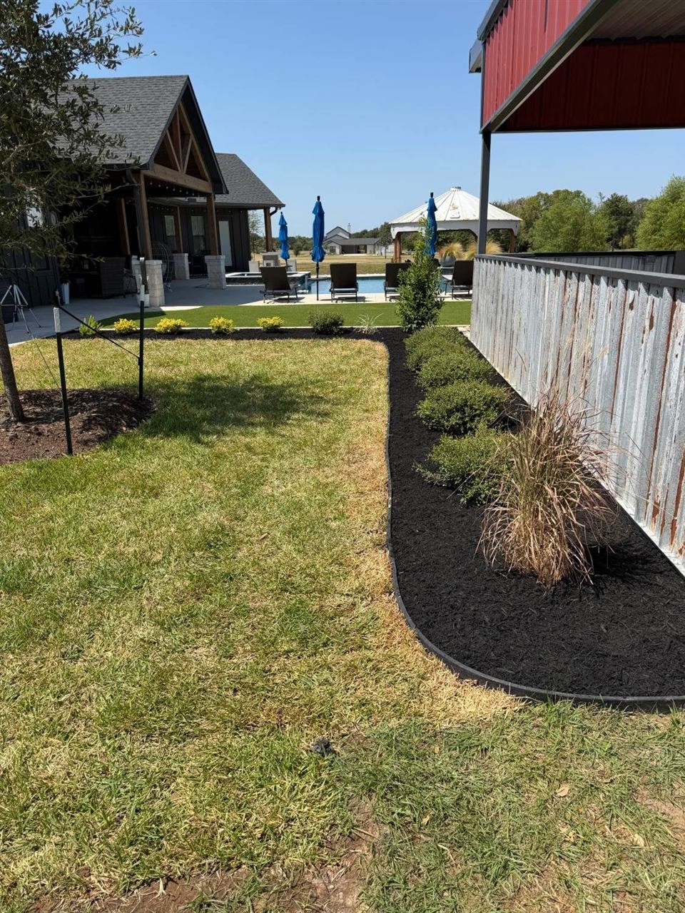 Black mulch bed with shrubs beside a backyard pool